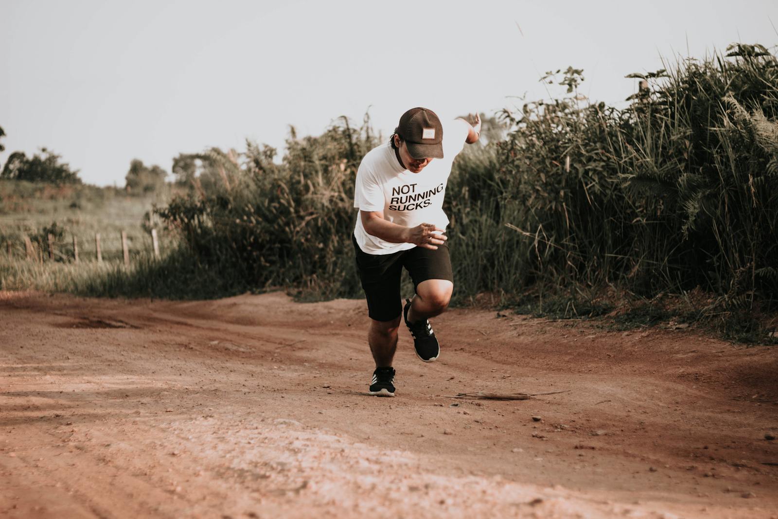 A man in sporty attire running on a rural dirt road with vegetation.