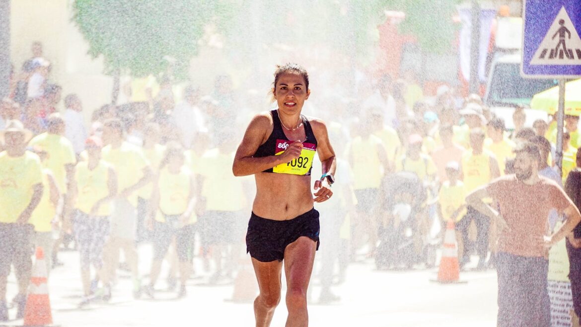A female athlete running in a marathon with a crowd cheering on a sunny day.