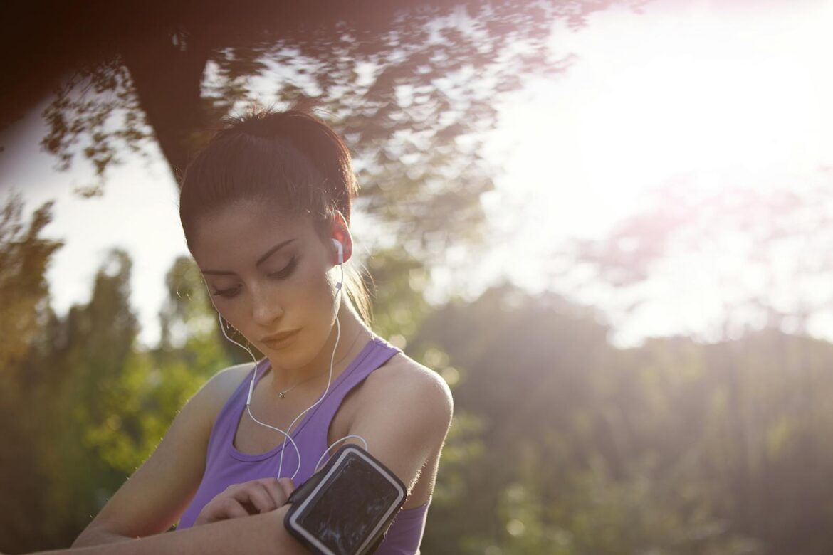 A young woman jogger enjoying music outdoors, wearing sportswear and a smartphone armband.