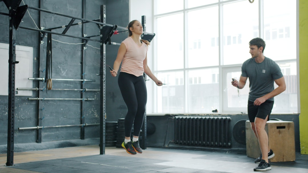 Active young woman is jumping with skipping rope training with male trainer in gym concentrated on exercise. Youth, workout and sports concept.