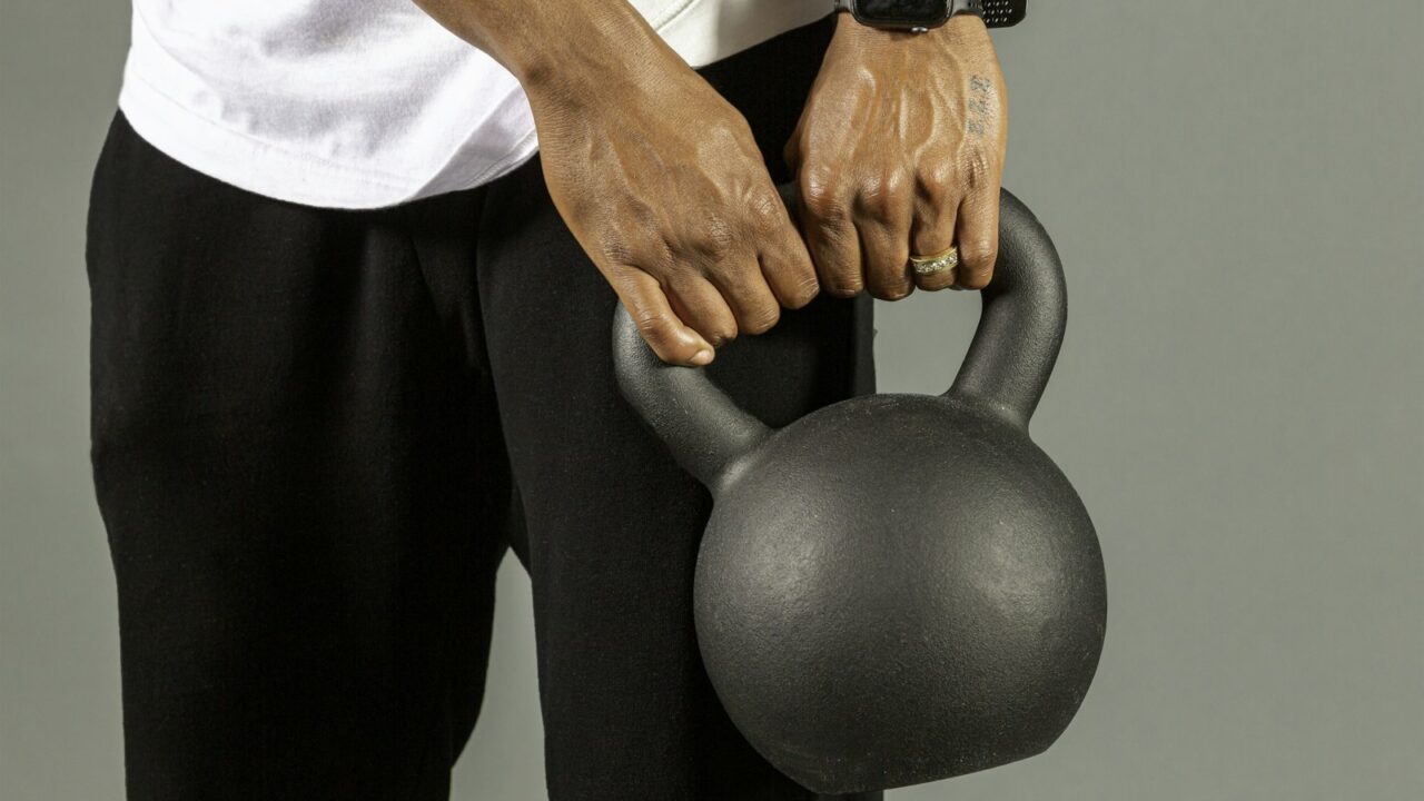 Oudere hardloper doet een krachtoefening met een kettlebell op een grasveld