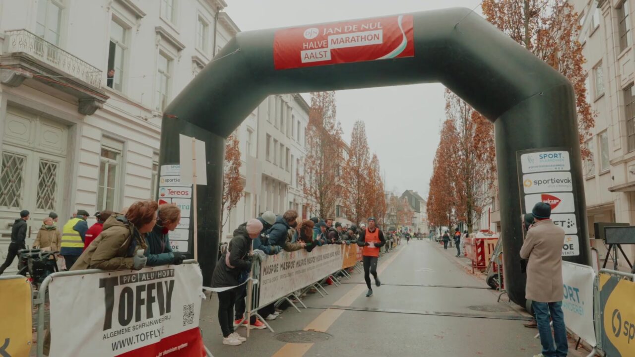 Een loper komt onder de finishboog van de halve marathon van Aalst door, met publiek langs de dranghekken