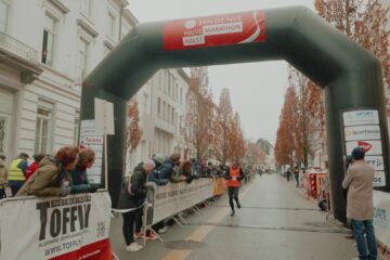 Een loper komt onder de finishboog van de halve marathon van Aalst door, met publiek langs de dranghekken