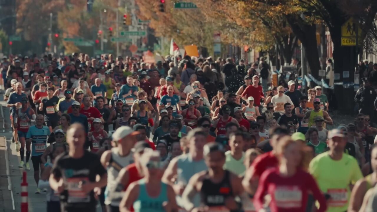 Een breed veld marathonlopers in een straat met herfstbomen tijdens de marathon van New York