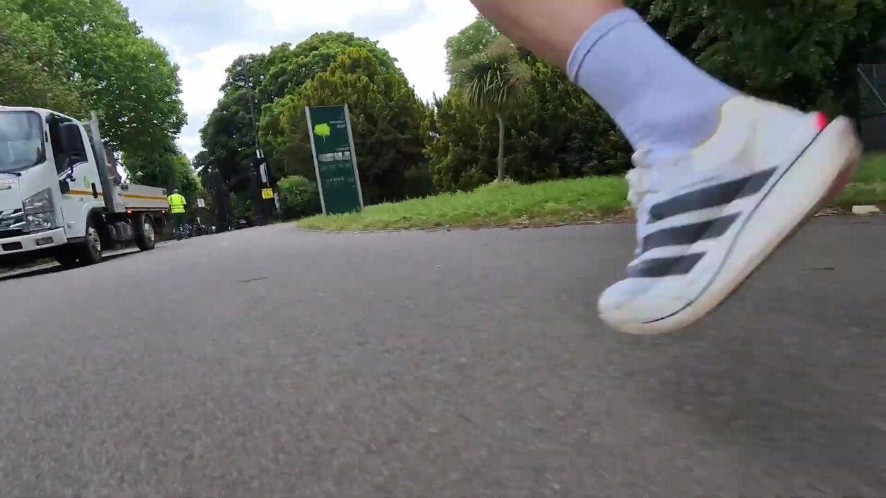 Close-up van een witte Adidas raceschoen tijdens het hardlopen op asfalt