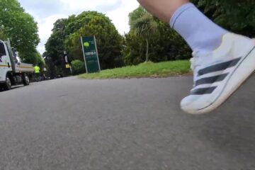 Close-up van een witte Adidas raceschoen tijdens het hardlopen op asfalt
