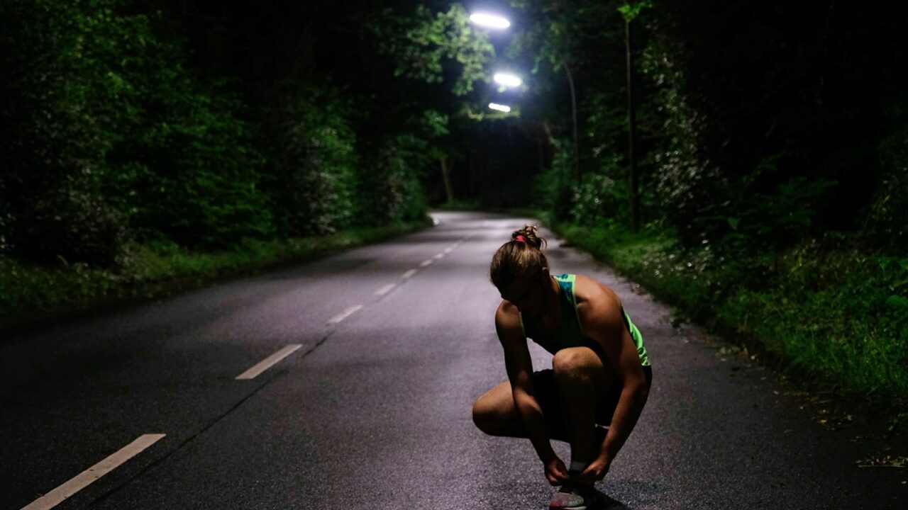 Hardloper met reflecterende kleding op een verlichte straat in de avondschemering